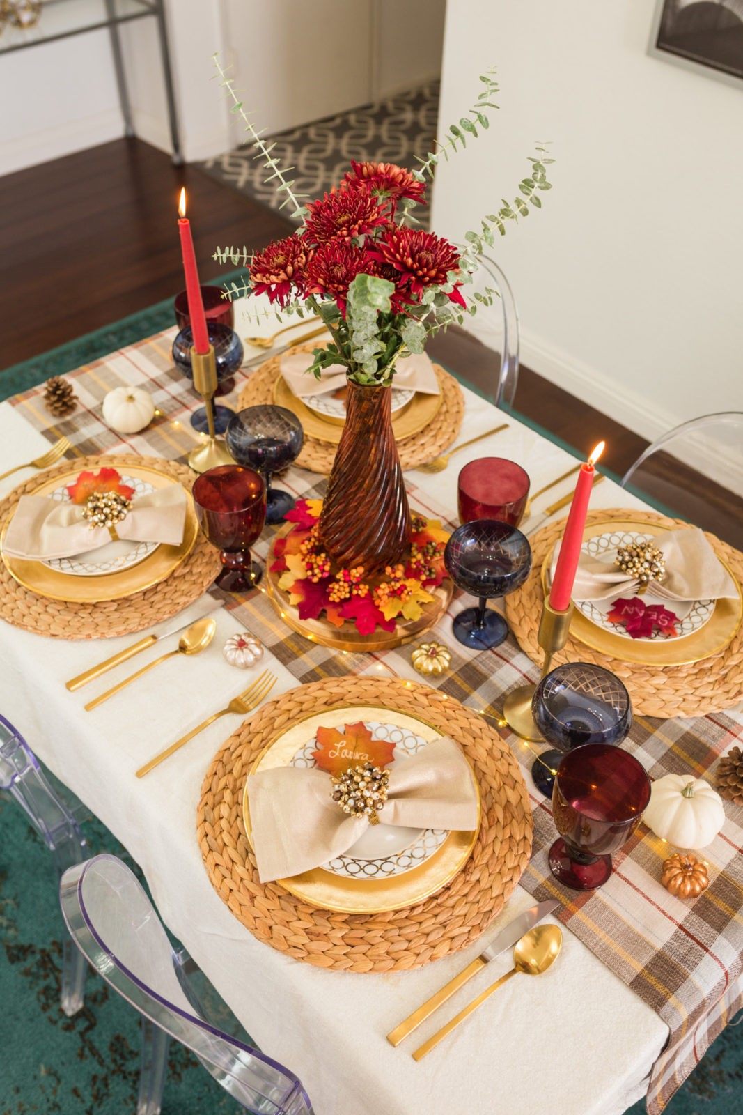 Easy Thanksgiving Table Setting Ideas by Lifestyle Blogger Laura Lily | Dinner Party Essentials: Hosting Tips, Table Settings Ideas and Bar Cart Inspiration by popular Los Angeles life and style blogger, Laura Lily: image of a table set with red candles, woven placemats, plaid table runner, gold plates, gold flatware, and red and blue glasses.