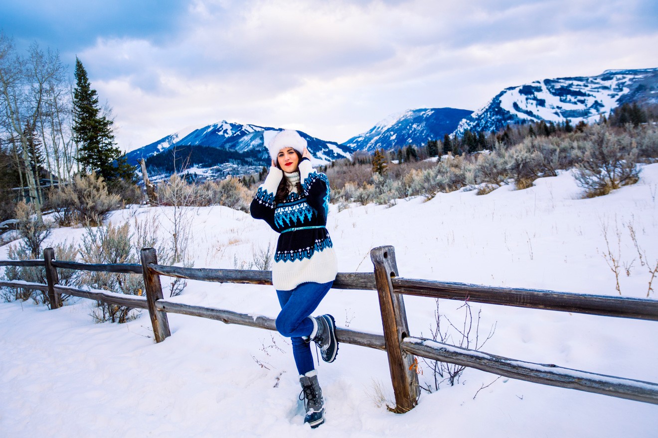 Ski Resort Style by Fashion Blogger Laura Lily, Topshop Fair Isle Sweater | How to Take Good Travel Photos by popular California travel blogger, Laura Lily: image of a woman standing outside in the snow and leaning up against a fence in Aspen, Colorado.