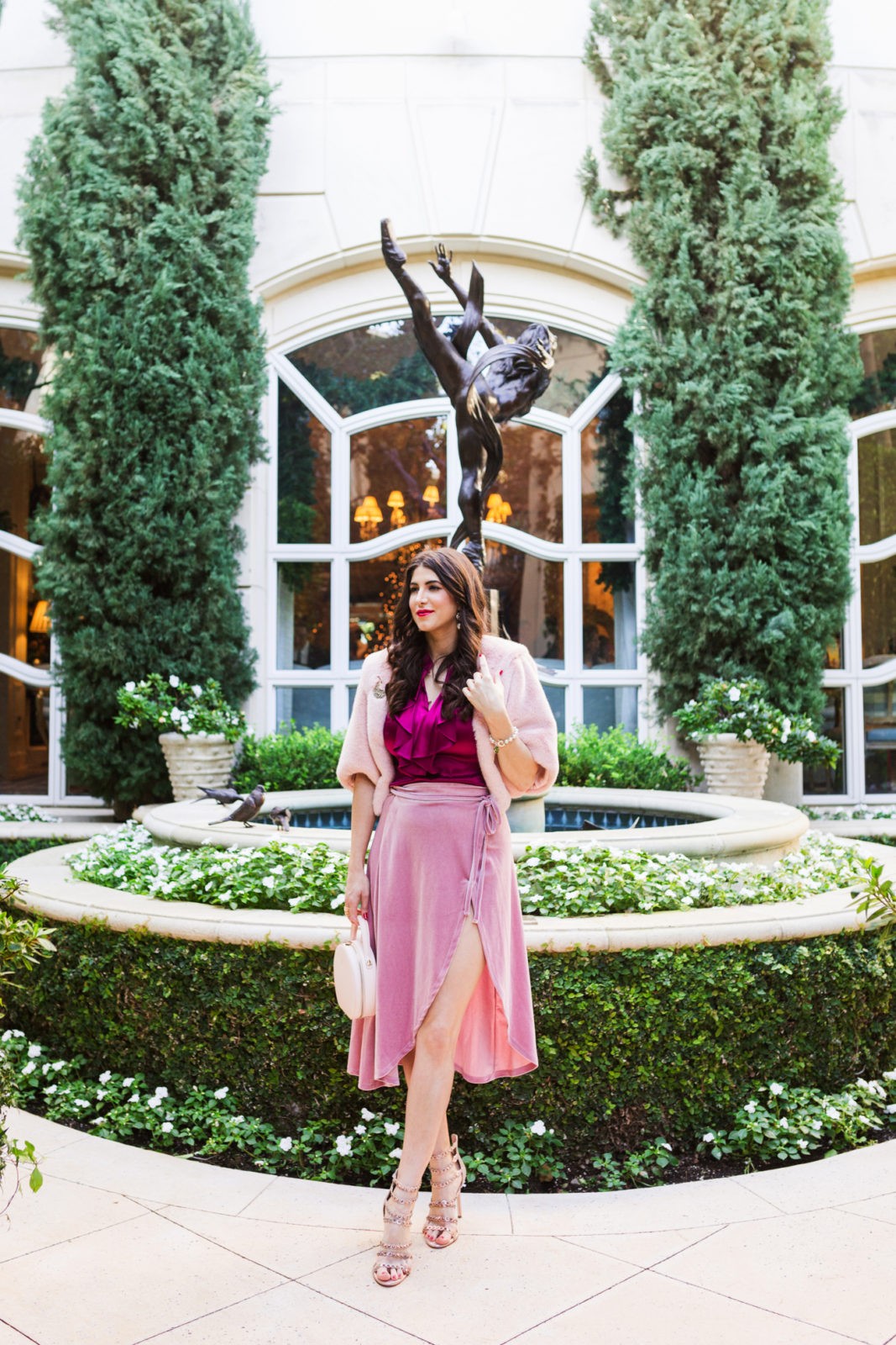 Pink Velvet wrap skirt styled for Spring by top US fashion blogger, Laura Lily: image of a woman wearing an ASOS velvet wrap skirt, Jessica Simpson heels, The Daily Edit engraved bag, Express top and Eliza J faux fur caplet at the Peninsula Beverly Hills Hotel