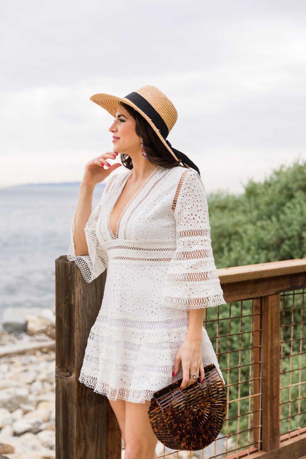 Vacation Outfit Ideas featured by top US fashion blogger Laura Lily; Image of a woman wearing a Red Dress Boutique White Eyelet Dress, Red Dress Boutique acrylic handbag, Dolce Vita sandals and BaubleBar Earrings.