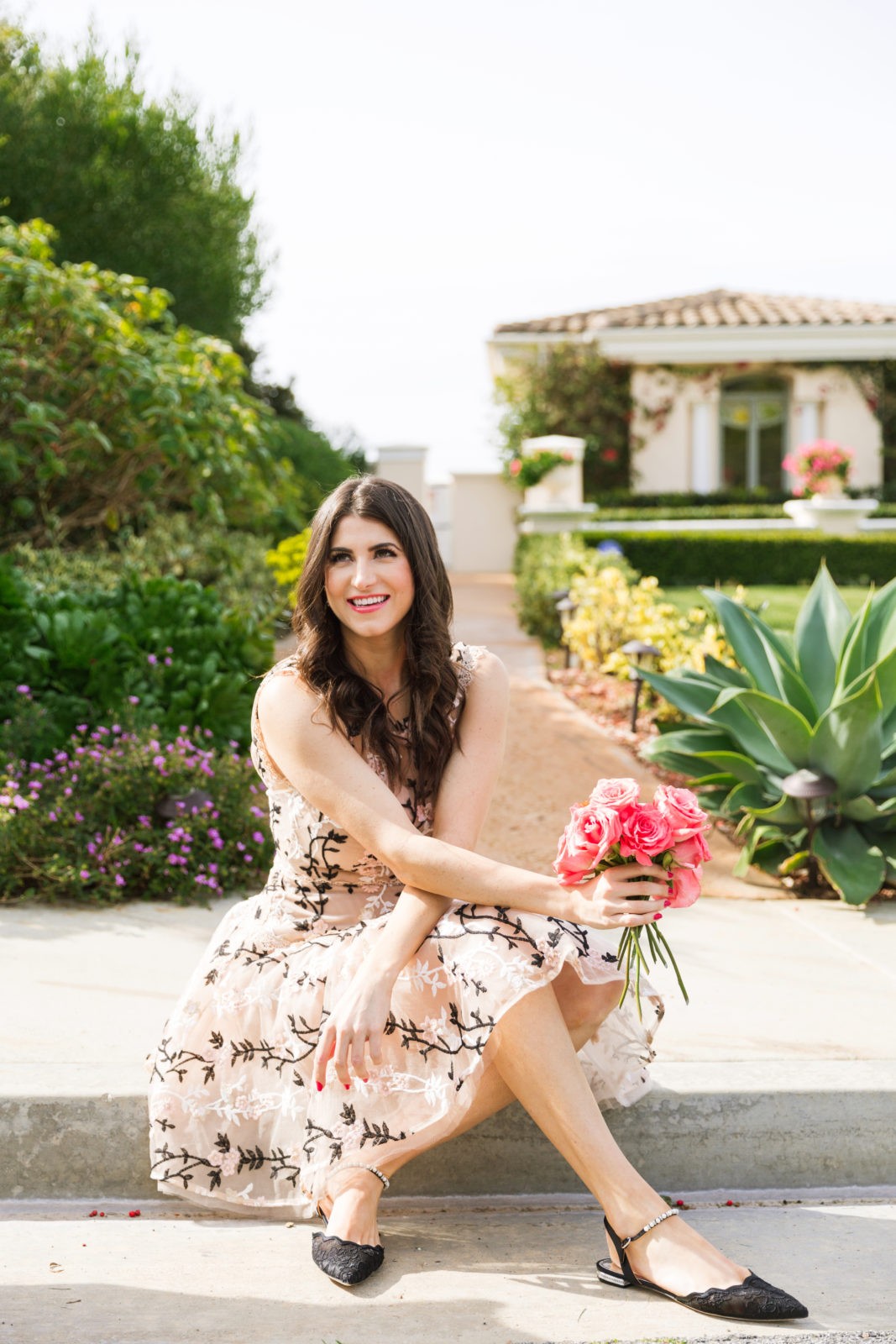 Designer Highlight: Bronx and Banco by popular Los Angeles Fashion Blogger Laura Lily: image of woman wearing Cloe Embroidered mini dress sitting outside and holding a bouquet of pink roses. 