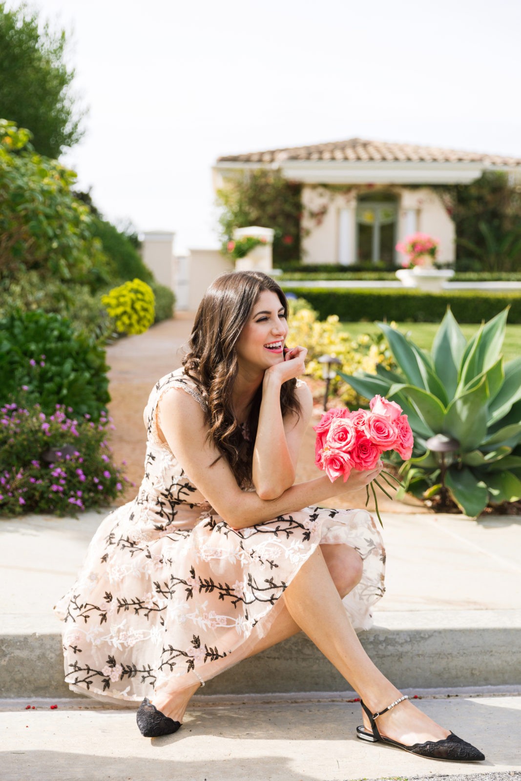 Designer Highlight: Bronx and Banco by popular Los Angeles Fashion Blogger Laura Lily: image of woman wearing Cloe Embroidered mini dress sitting outside and holding a bouquet of pink roses. 