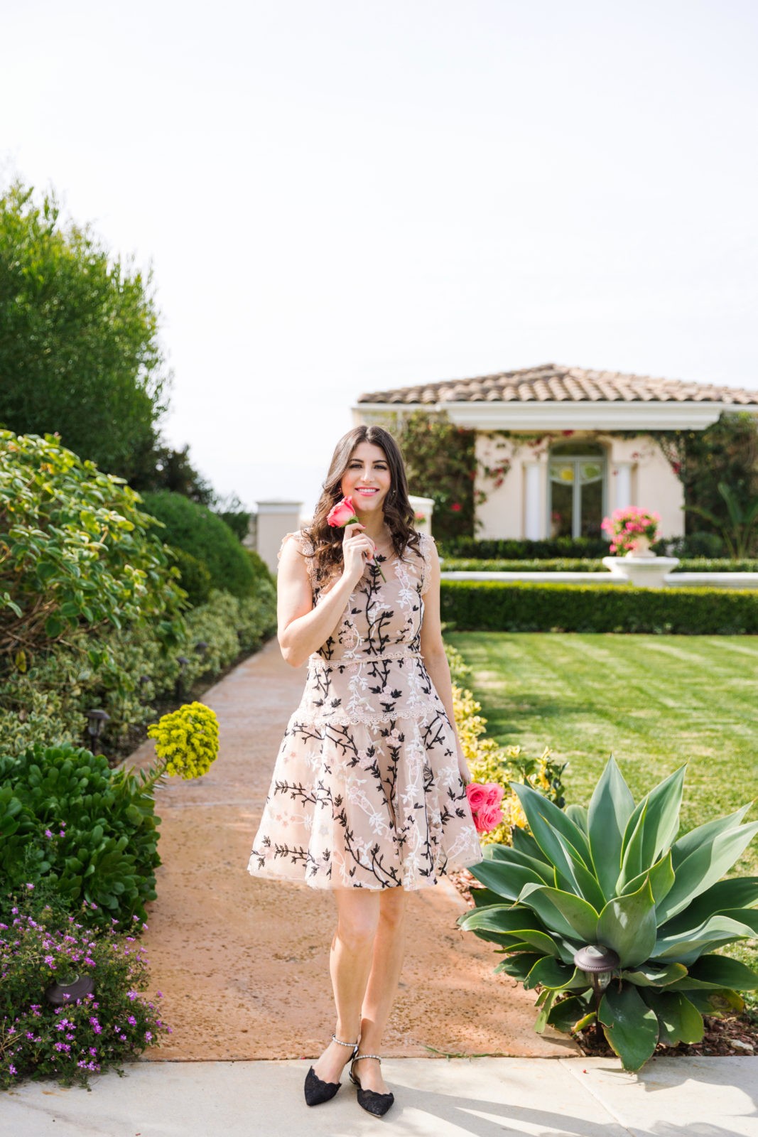 Designer Highlight: Bronx and Banco by popular Los Angeles Fashion Blogger Laura Lily: image of woman wearing Cloe Embroidered mini dress standing outside and holding a bouquet of pink roses. 