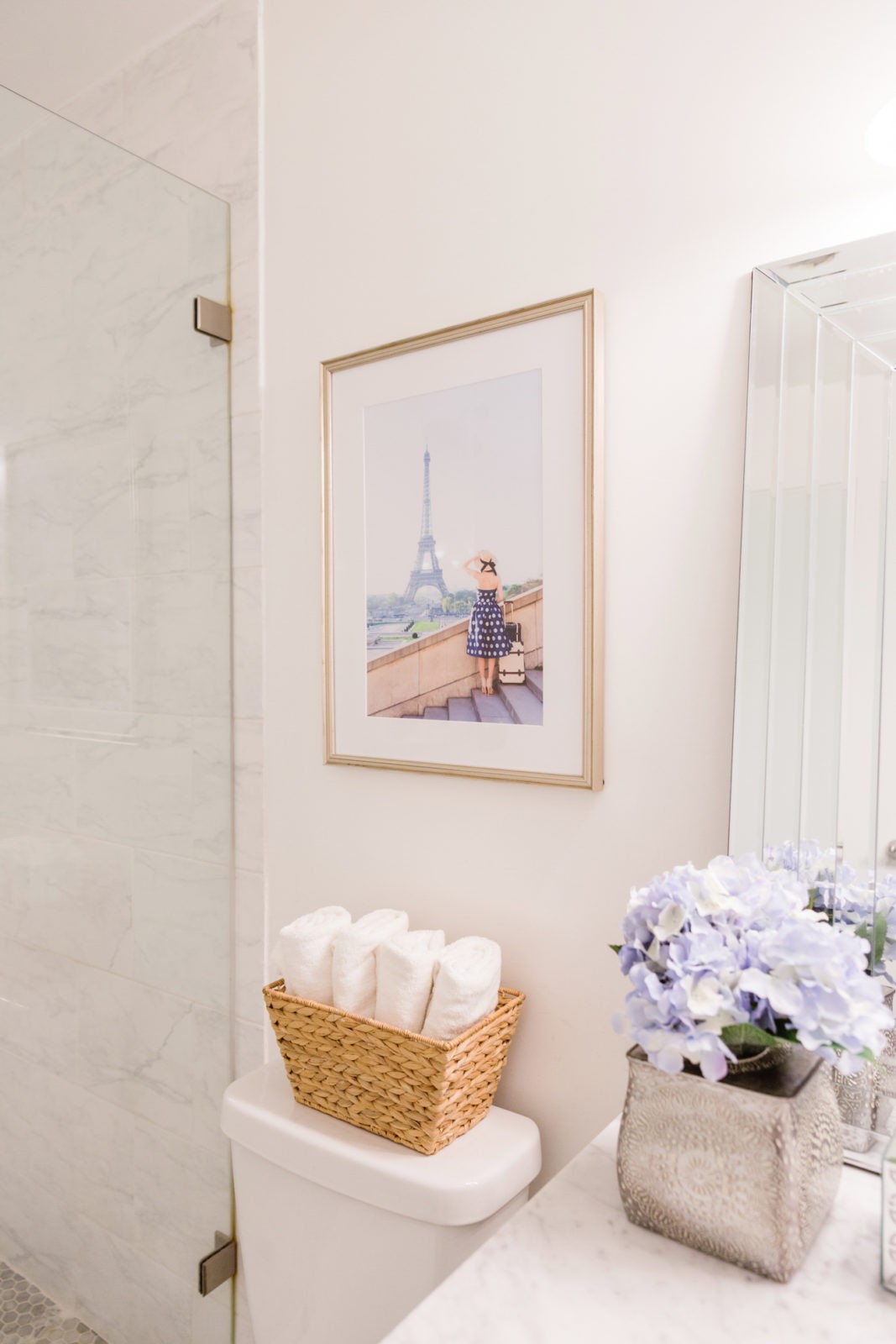 Modern Bathroom Remodel Ideas + Reveal featured by popular US lifestyle blogger, Laura Lily: image of after photo of modern bathroom remodel framebridge photo, metal vase with flowers, and wicker basket holding rolled up white hand towels. 
