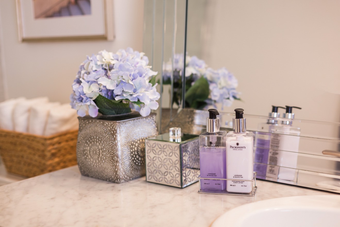 Modern Bathroom Remodel Ideas + Reveal featured by popular US lifestyle blogger, Laura Lily: image of marble vanity countertop with purple soap and lotion dispenser, metal vase with flowers, and metal container sitting on top. 