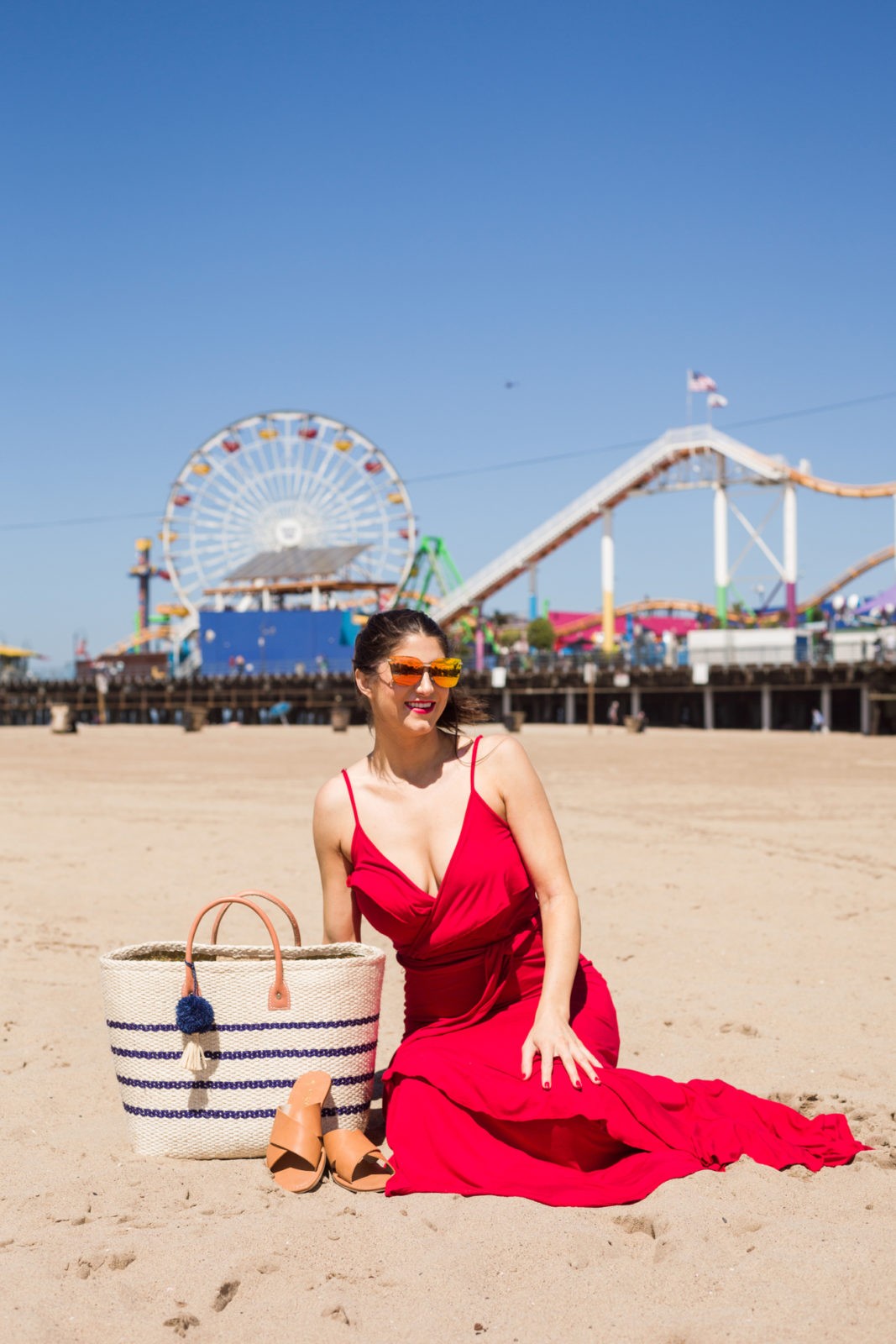 Cute Summer Dresses Under 50, Summer Fashion Trends Walmart We Dress America by popular Los Angeles Fashion Blogger Laura Lily: image of woman at the beach wearing red Walmart faux wrap front maxi dress , Walmart Prive Revaux sunglasses, Melrose Ave vegan brown slide sandals, and Eliza May woven blue stripe tote.