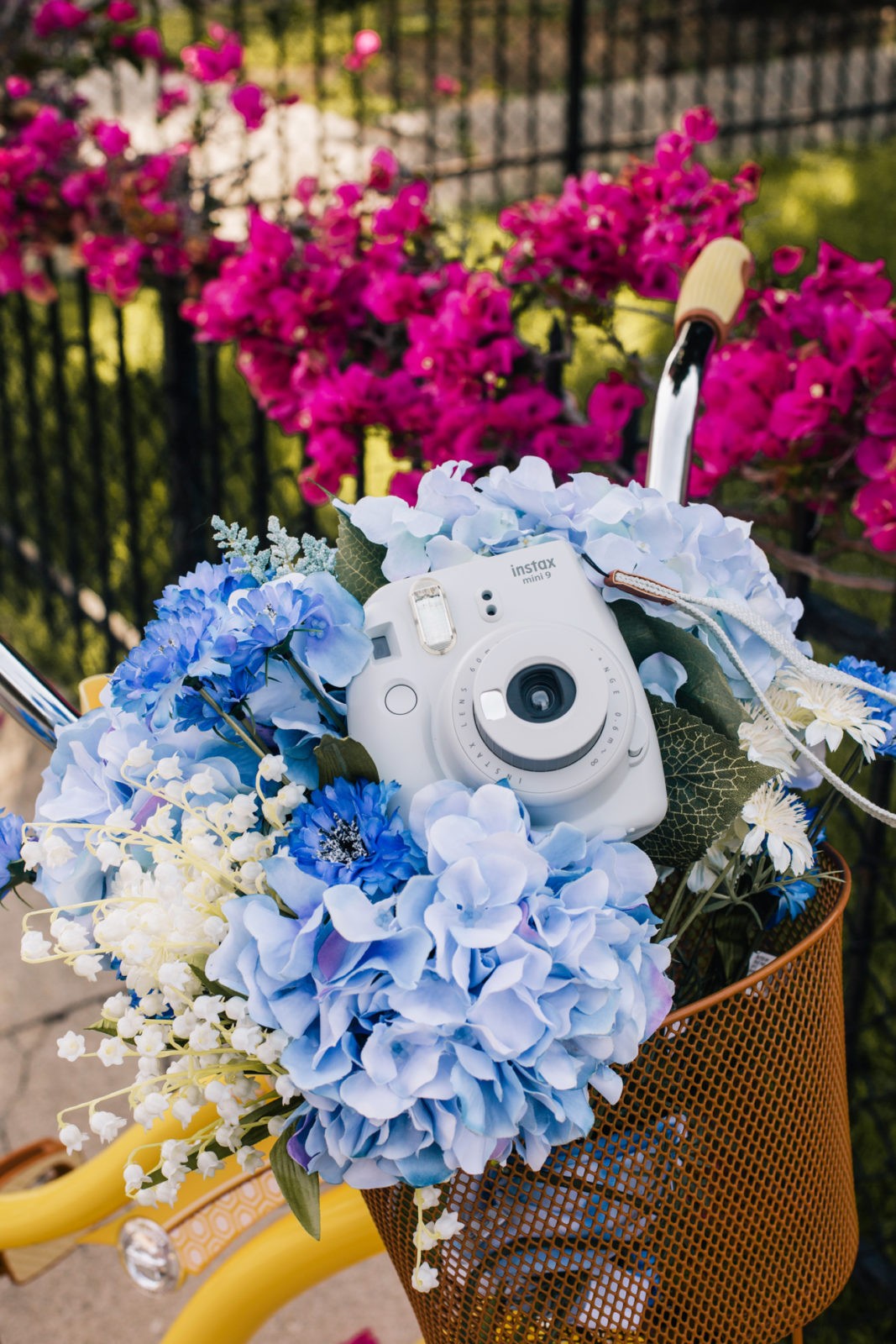 Stage Summer Moments, 2019 Summer Bucket List Moments by popular Los Angeles Lifestyle Blogger Laura Lily: image of Stage Stores yellow beach cruiser bike with bike basket full of flowers and gray Polaroid Instax mini camera.