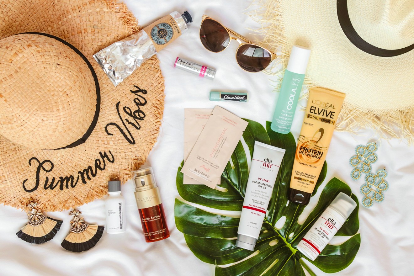 Essential Skincare Travel Products by Travel Blogger Laura Lily: image of straw sun hat, sunglasses, gold earrings, and various travel skincare products.