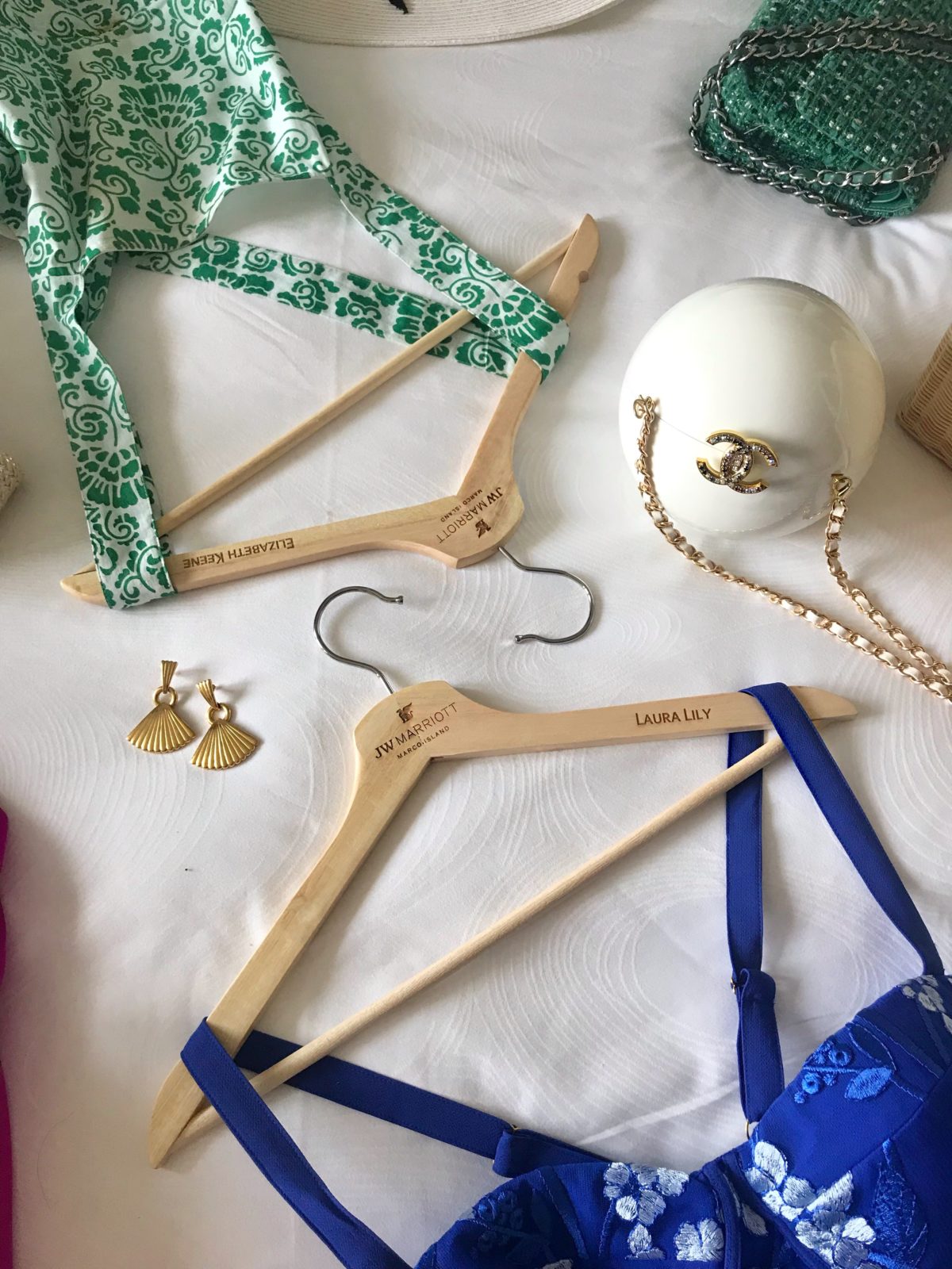 JW Marriott Marco Island by Luxury Travel Blogger Laura Lily: image of a Channel purse, gold drop earrings, and two dresses laid out on a bed.