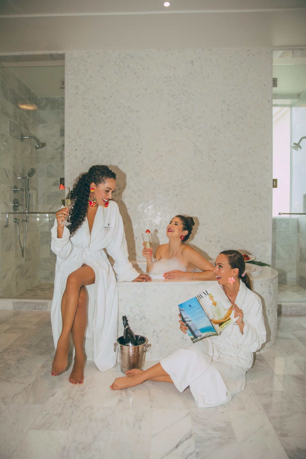 JW Marriott Turnberry Resort Miami by popular travel blogger, Laura Lily: image of a woman and her two friends sitting by a tub with bubbles in it while they drink champagne. 