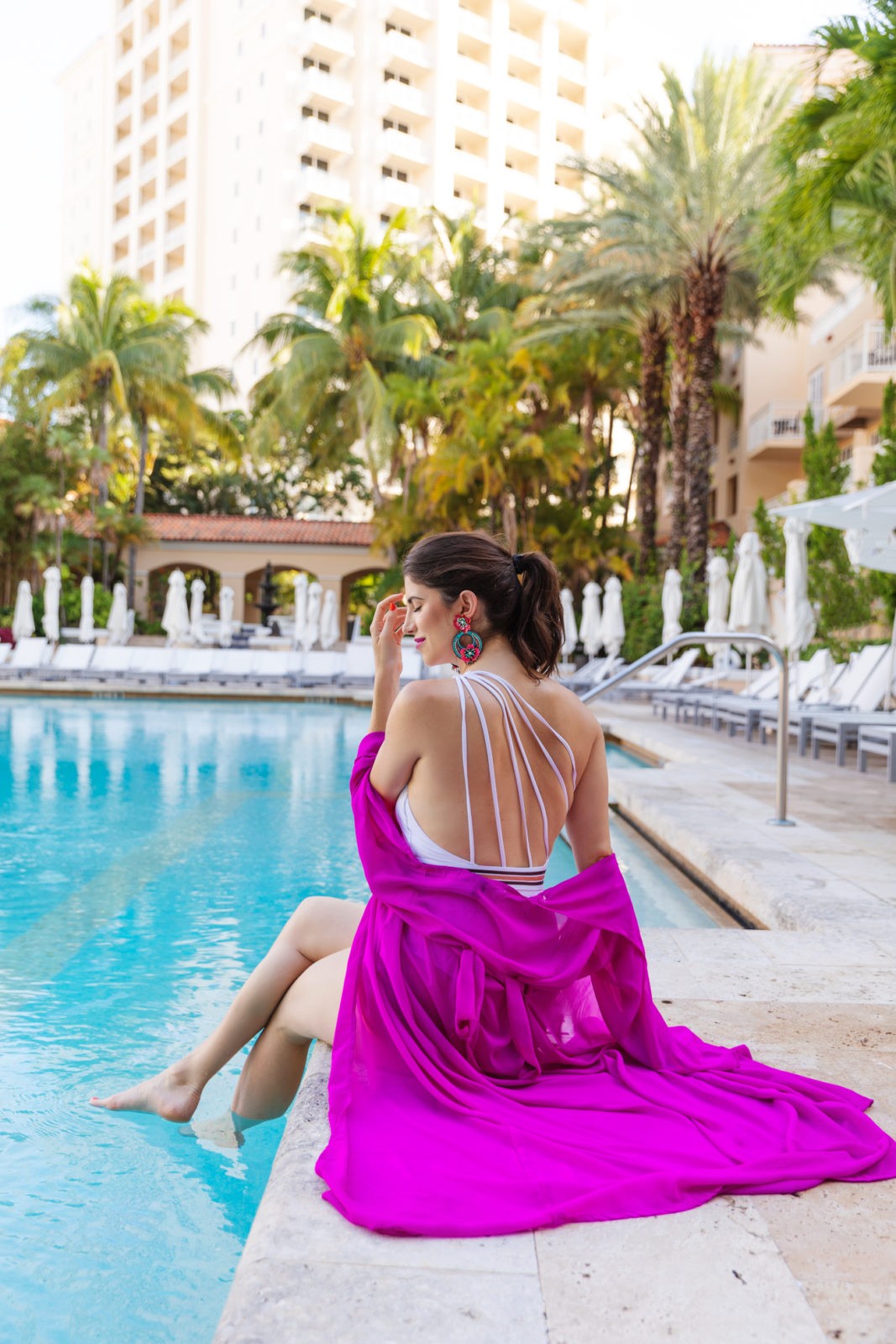 JW Marriott Turnberry Resort Miami by popular travel blogger, Laura Lily: image of a woman sitting at the edge of the pool with her feet in the water.