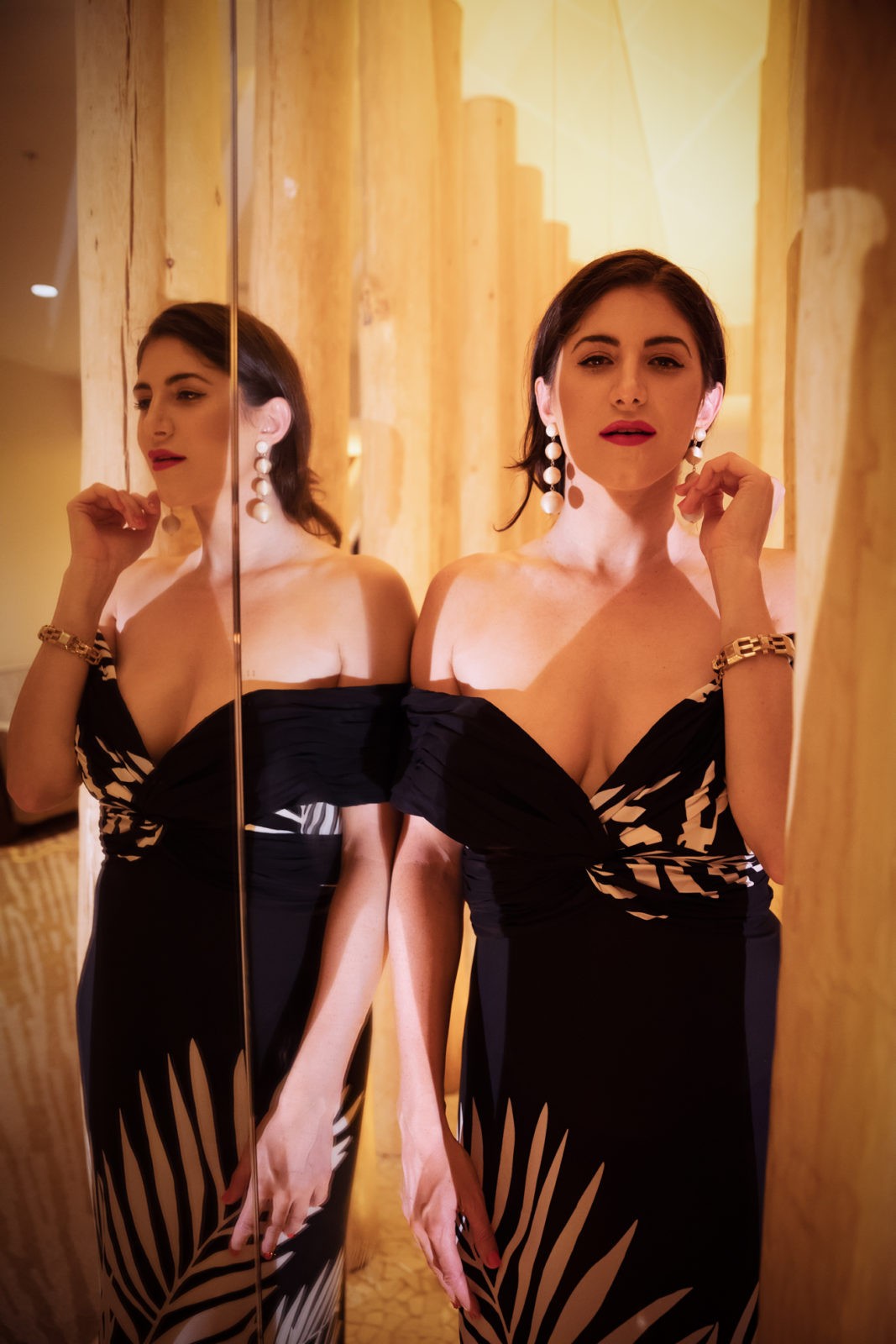 iJW Marriott Marco Island by Luxury Travel Blogger Laura Lily: image of a woman standing next to a full length mirror and wearing a black and white palm leaf print off-shoulder dress and large pearl drop earrings.