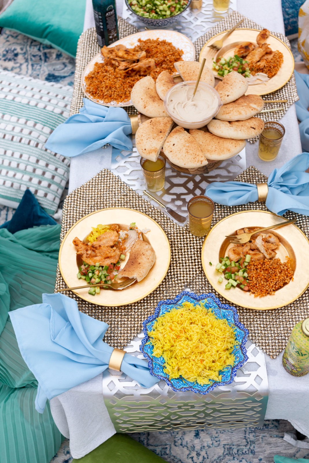 Moroccan Picnic with Atay Tea by popular California life and style blogger, Laura Lily: image of a moroccan picnic at the beach with gold beaded placemats, various moroccan foods, blue and green pillows, blue linen napkins, gold embellished moroccan cups, gold plate, gold silverware, and Atay Tea.