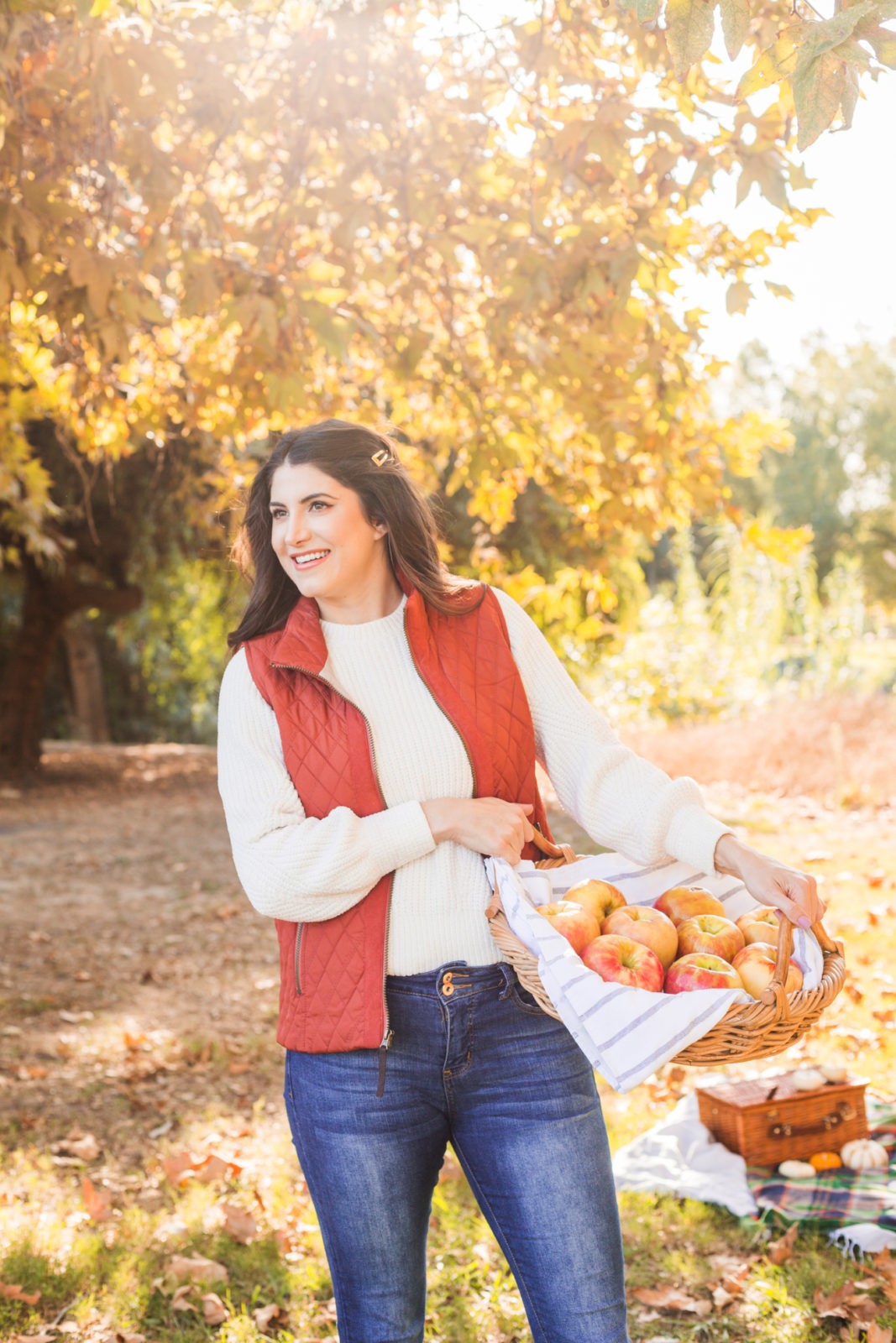 Cozy Fall Favorites by Los Angeles Fashion Blogger Laura Lily | Cozy Fall Fashion Trends by popular California fashion blogger, Laura Lily: image of a woman holding a basket of apples outside and wearing a H&M Chenille Sweater, jeans, Born Boots, and a quilted vest.