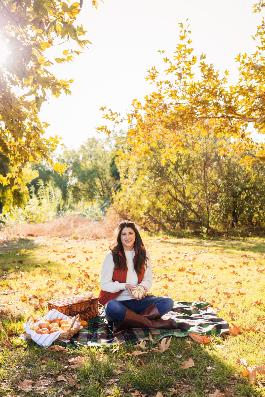 Cozy Fall Favorites by Los Angeles Fashion Blogger Laura Lily | | Cozy Fall Fashion Trends by popular California fashion blogger, Laura Lily: image of a woman sitting on a picnic blanket outside while holding a pumpkin and wearing a H&M Chenille Sweater, jeans, Born Boots, and a quilted vest.