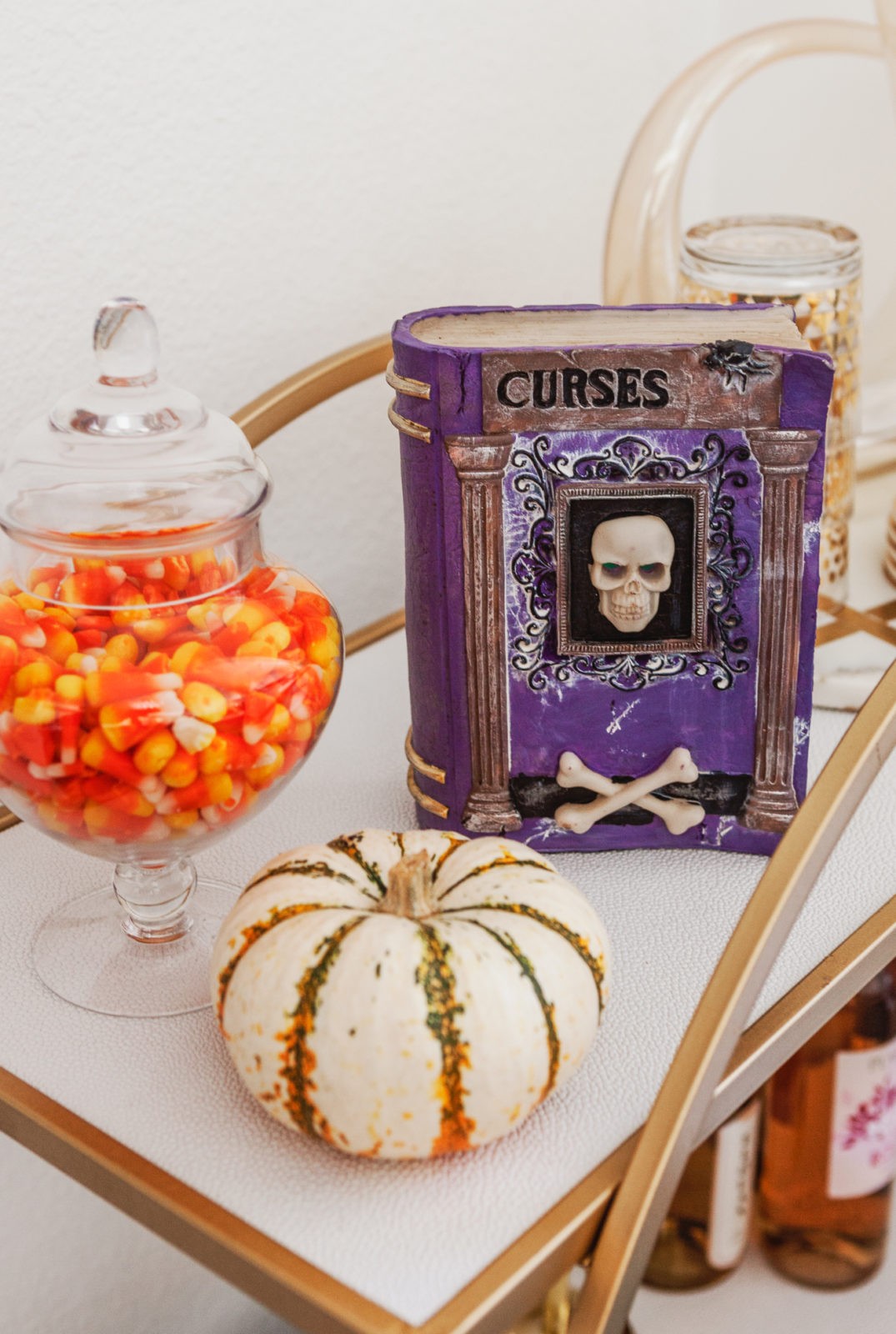 Halloween Themed Bar Cart and Party Ideas by Los Angeles Lifestyle Blogger Laura Lily | Halloween Bar Cart Ideas by popular Los Angeles life and style blogger, Laura Lily: image of a Z Gallerie Russo Bar Cart that's decorated with faux pumpkins, faux fall leaves, Halloween spell book, apothecary jars with candy corns, wine glasses, and liquor. 