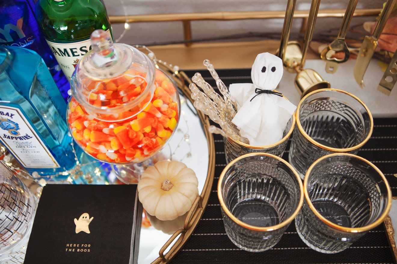 Halloween Themed Bar Cart and Party Ideas by Los Angeles Lifestyle Blogger Laura Lily | Halloween Bar Cart Ideas by popular Los Angeles life and style blogger, Laura Lily: image of a Z Gallerie Russo Bar Cart that's decorated with faux pumpkins, faux fall leaves, Halloween spell book, apothecary jars with candy corns, wine glasses, tumbler glasses and liquor. 