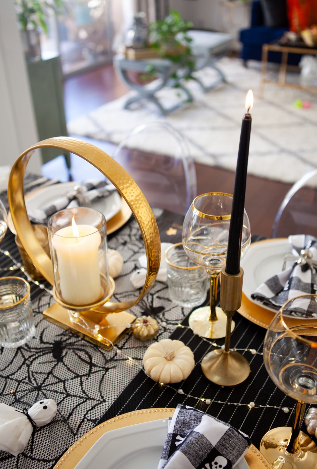 Fun and Easy Halloween Tablescape Decorating Ideas by Home Decor Blogger Laura Lily | Fun and Easy Halloween Table Decor Ideas by popular California lifestyle blogger, Laura Lily: image of table decorated with black candlesticks, gold stem glassware, gold plate chargers, spider web tablecloth, black and white gingham napkins, and silver spider napkin rings. 