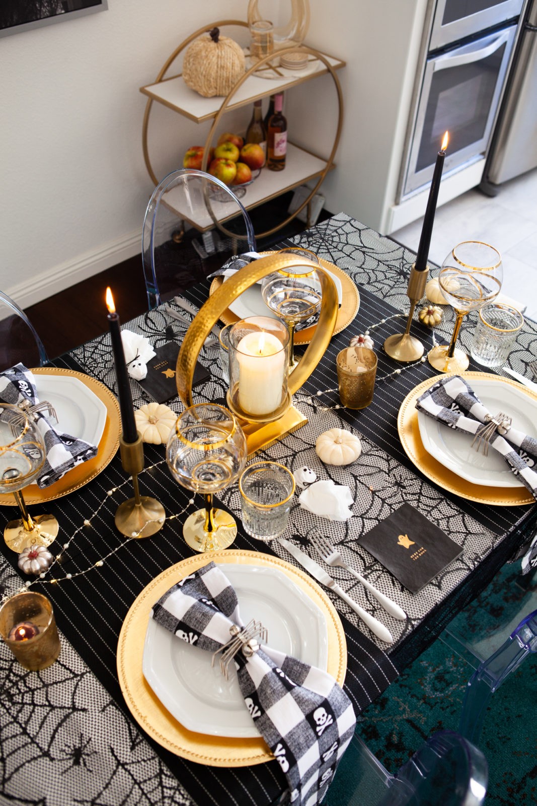 Fun and Easy Halloween Tablescape Decorating Ideas by Home Decor Blogger Laura Lily | Fun and Easy Halloween Table Decor Ideas by popular California lifestyle blogger, Laura Lily: image of table decorated with black candlesticks, gold stem glassware, gold plate chargers, spider web tablecloth, black and white gingham napkins, and silver spider napkin rings. 
